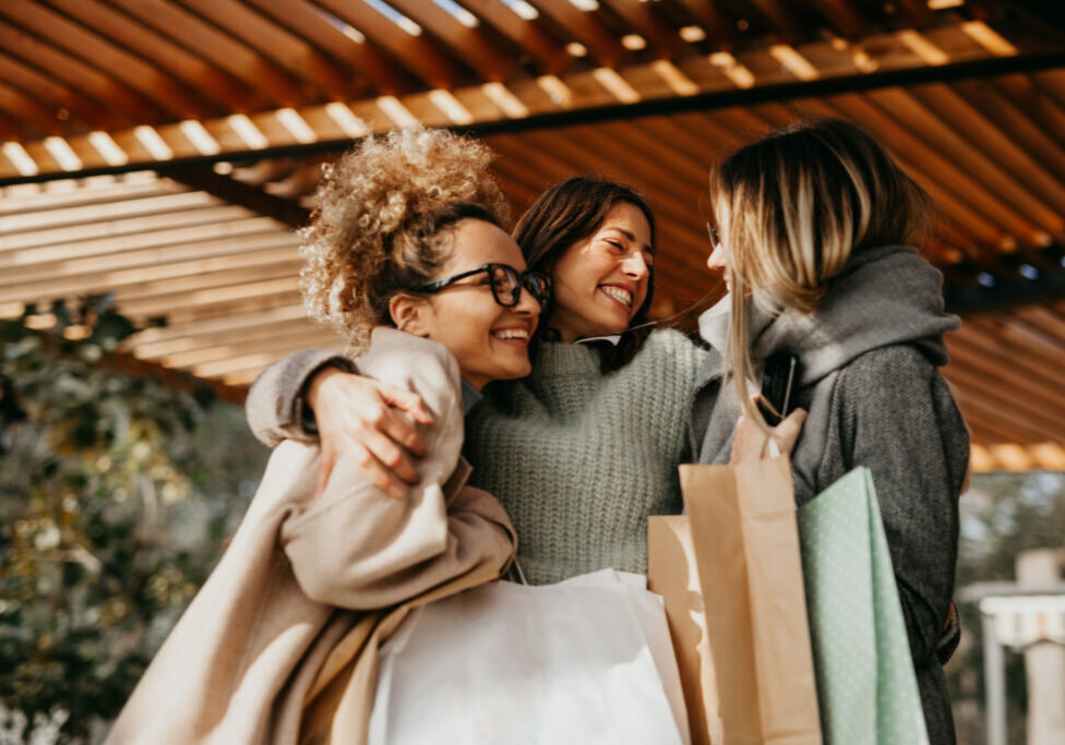 Small group of cheerful women friends embracing and walking into a cafeteria after shopping.