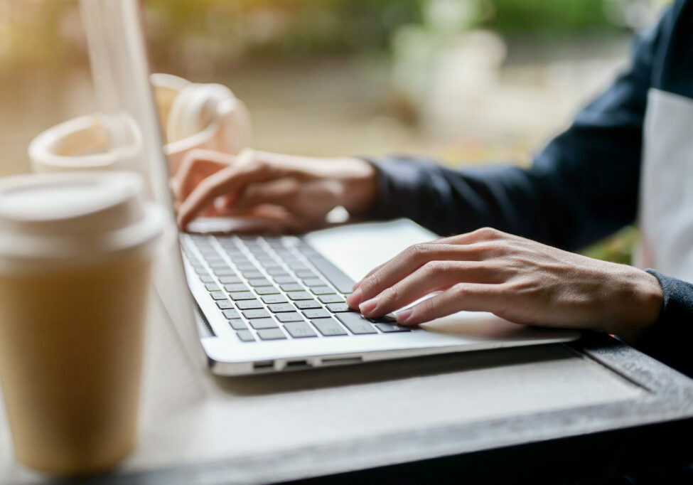 A close-up side view image of a man working remotely from an outdoor table, using his laptop computer, typing on the keyboard. people and technology concepts
