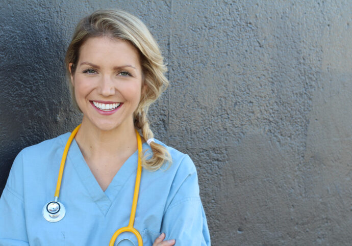Nurse with long blonde hair and a stethoscope in a uniform smiling at the camera.