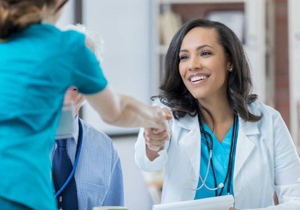 Beautiful mixed race doctor greets a nurse during job interview. The women are shaking hands.